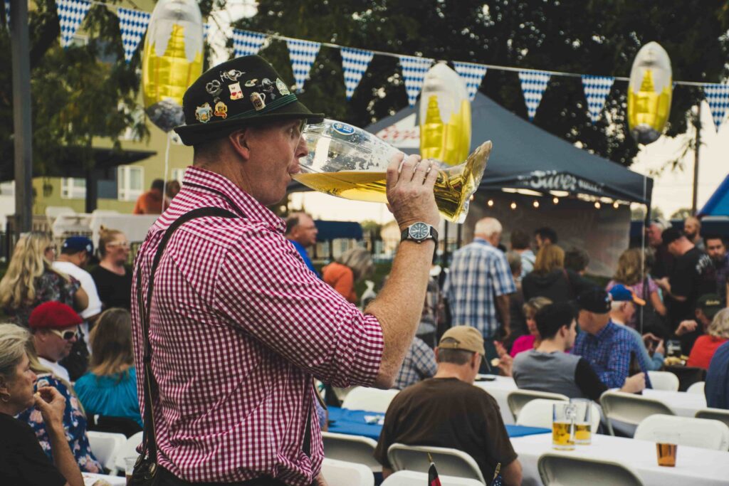 Man drinking from a boot-shaped beer glass. - Lederhosen For Sale