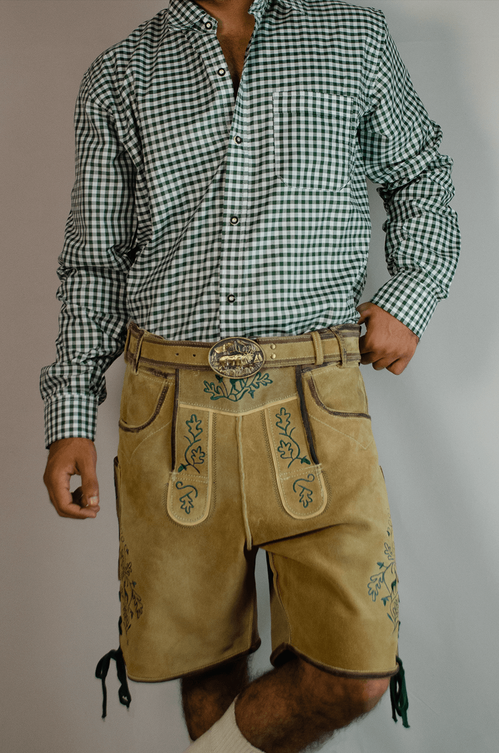 Man wearing light gold handcrafted Lederhosen shorts with a matching belt, large ornate buckle, and a green checkered shirt. - Lederhosen For Sale