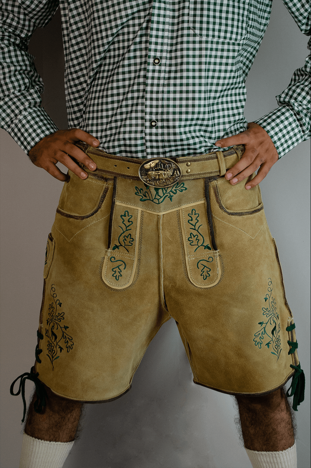 Front view of a man wearing light gold handcrafted Lederhosen shorts with detailed green oak leaf embroidery and a large ornate gold belt buckle. - Lederhosen For Sale