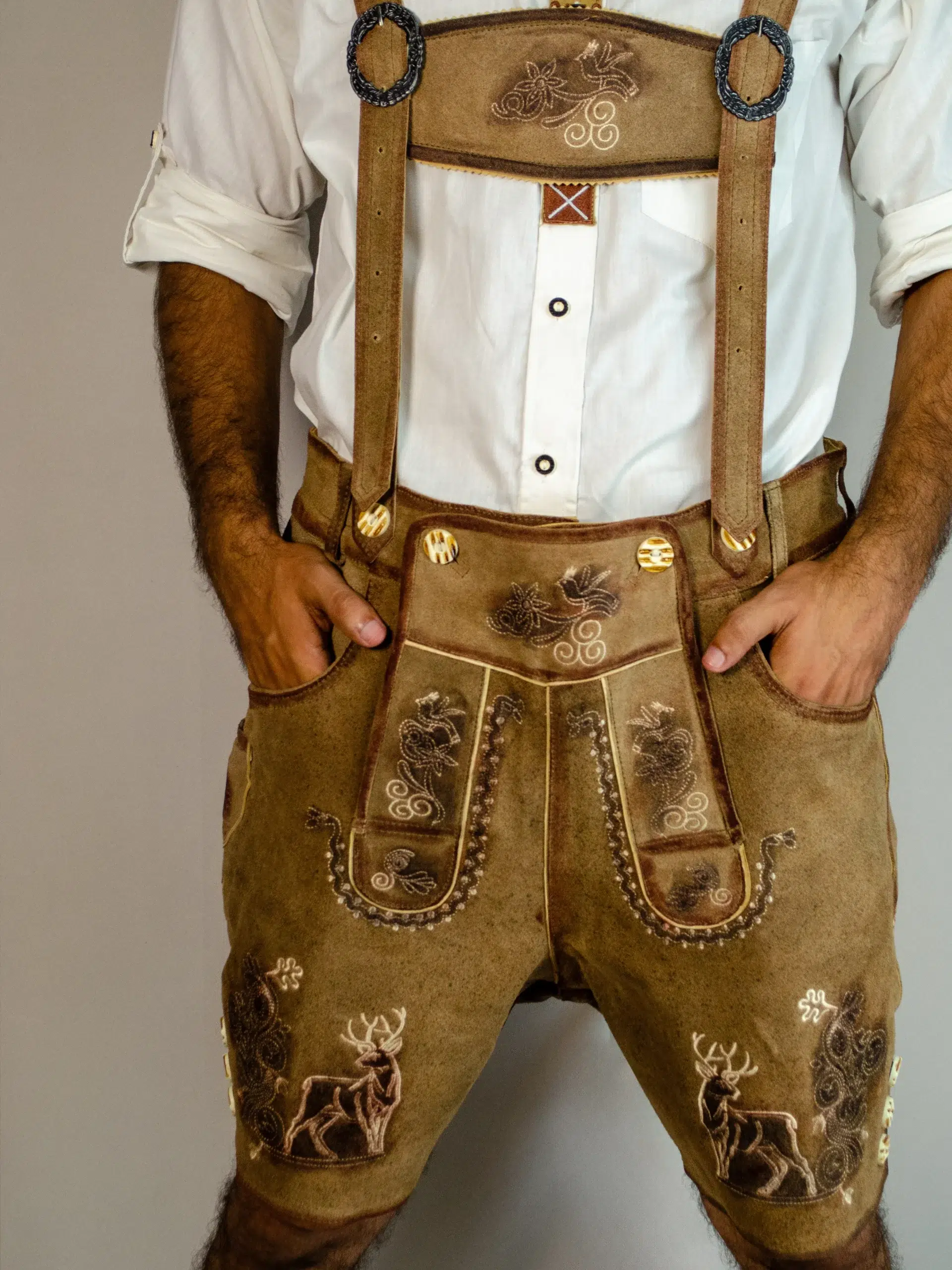 Front view of man with hands in pockets wearing tan embroidered Lederhosen. - Lederhosen For Sale