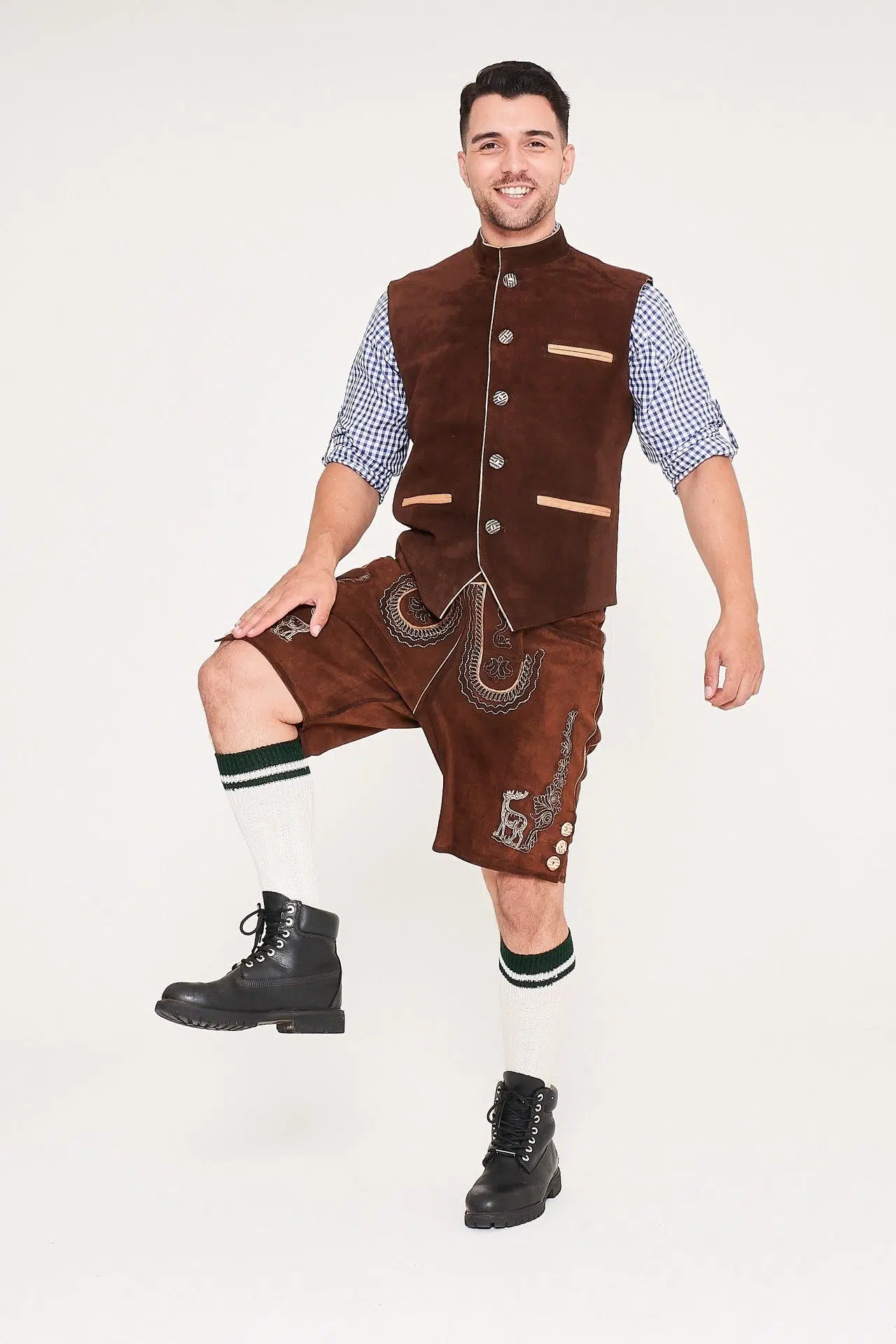 Front view of man posing with leg up in brown waistcoat, Lederhosen, and blue checkered shirt. - Lederhosen For Sale