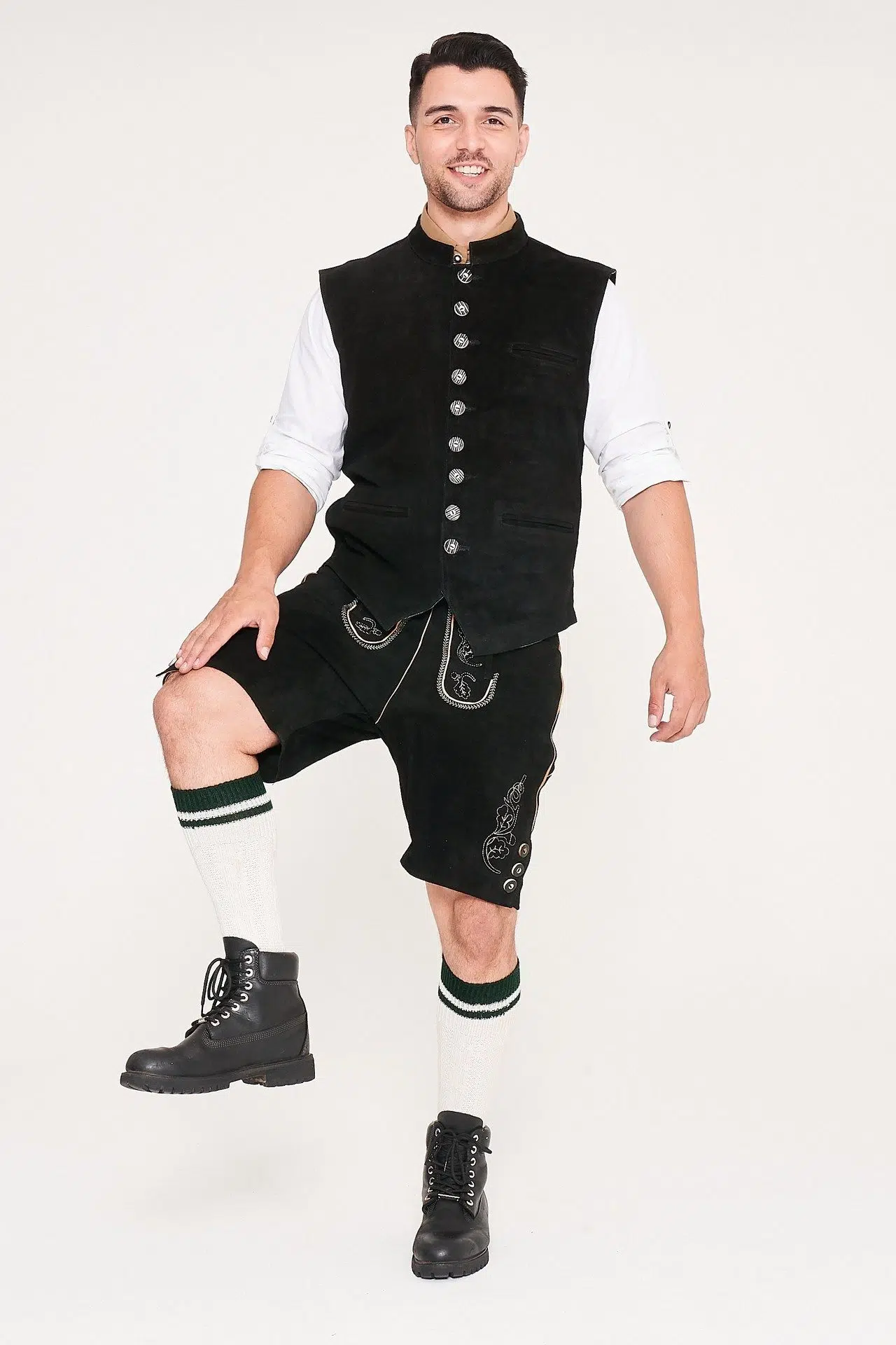 Front view of man posing with leg up in black waistcoat, Lederhosen, and white shirt. - Lederhosen For Sale