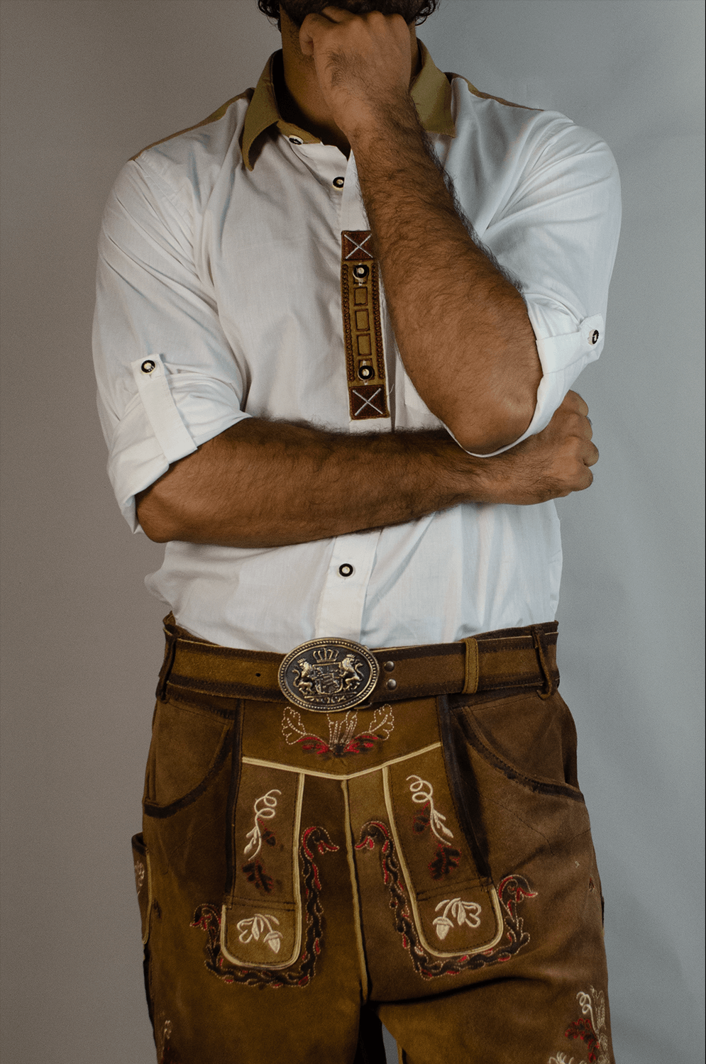 Man wearing traditional brown embroidered Lederhosen with an ornate silver crest belt buckle and a white shirt with tan collar trim. - Lederhosen For Sale